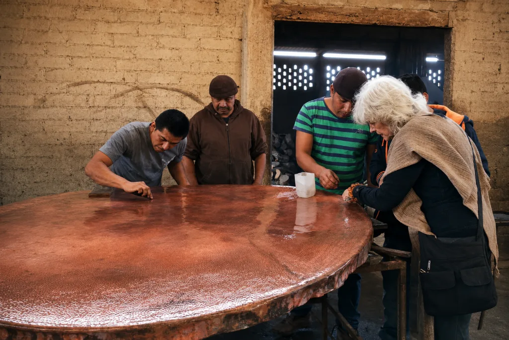 Teresa and four coppersmiths inspecting a large polished copper tabletop together
