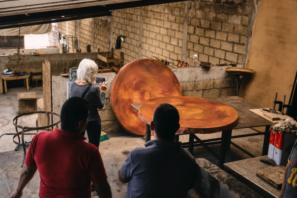 Teresa photographing two finished copper tabletops while two of the makers look on