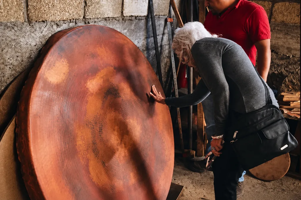 Teresa running her hand across the hammered surface of a large round copper tabletop
